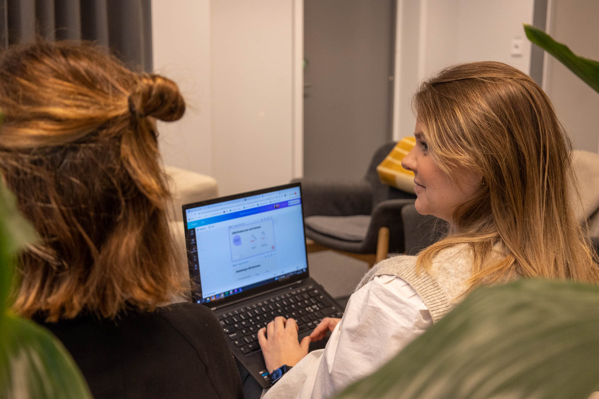 Två personer sitter med ryggen åt i en soffa och en ena personen har en laptop i knäet