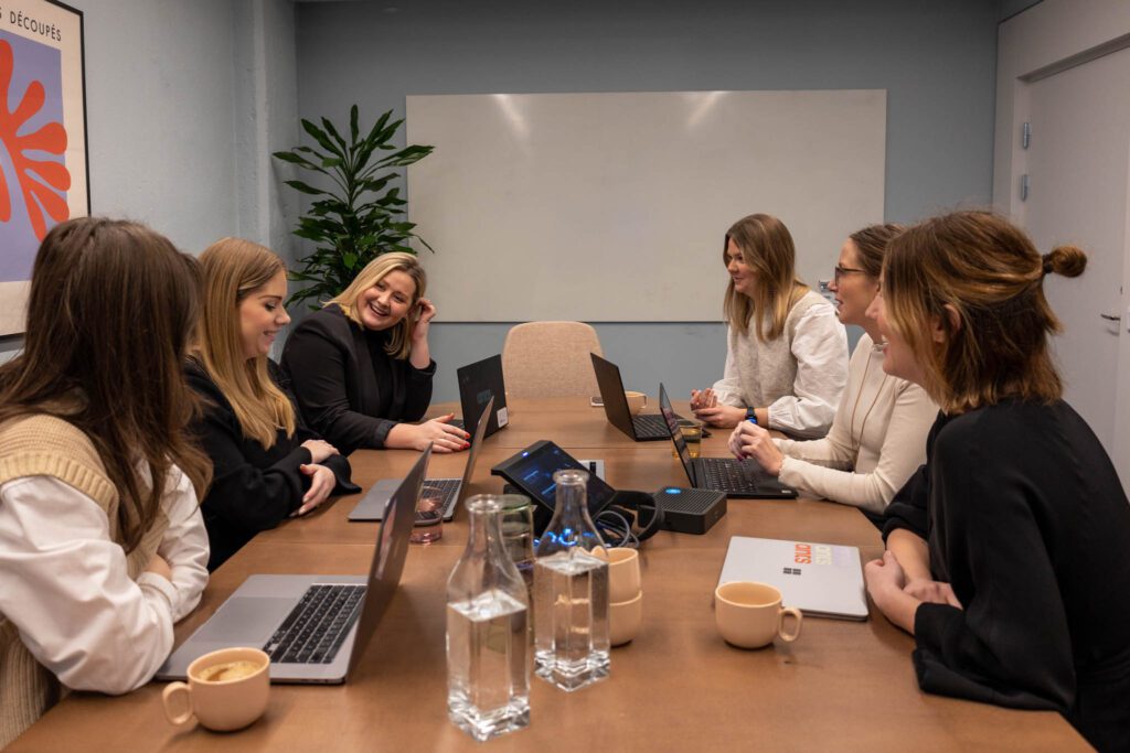 Personer sitter vid ett bord framför laptops och pratar om rollen Director of E-commerce.