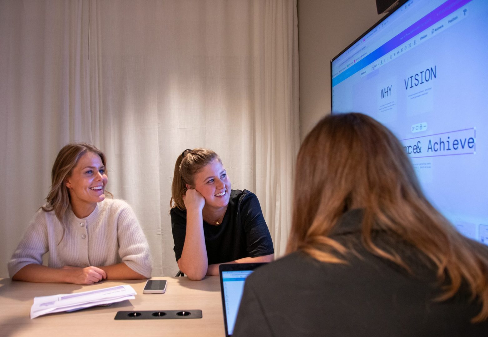 Tre konsulter sitter tillsammans i ett mötesrum och samtalar om IT-rekrytering. De sitter och tittar på en TV-skärm på väggen.