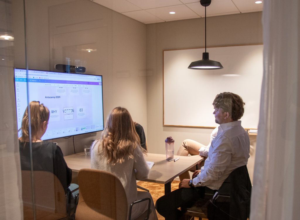 En grupp sitter i ett mötesrum och tittar på en TV skärm tillsammans. 