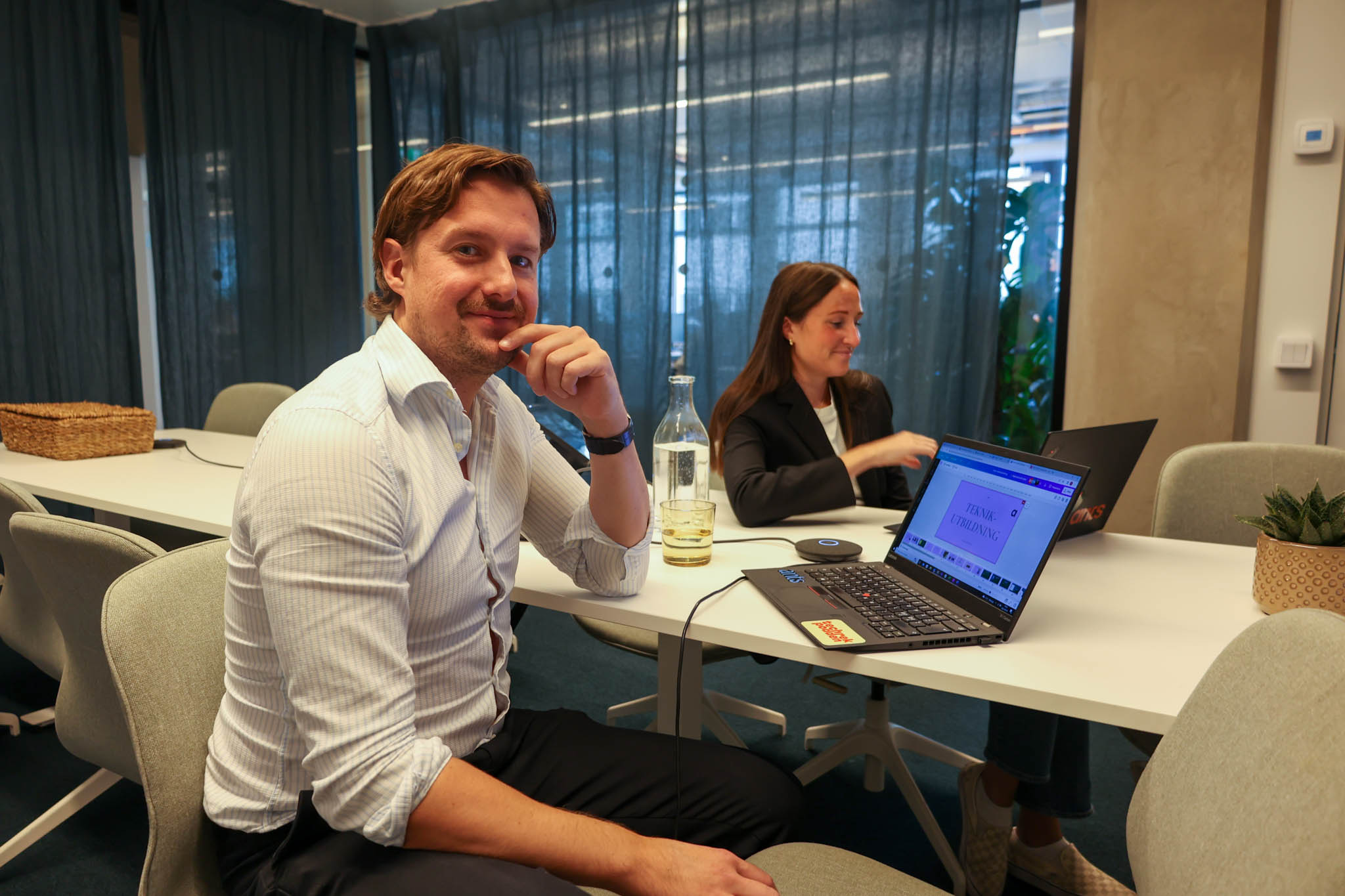 En Product Owner för Development Operations sitter i ett inglasat mötesrum med en kollega och diskuterar kontinuerlig integrationsutveckling för embedded software.