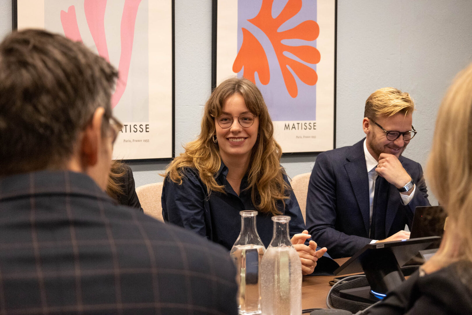 En glad CEO, Chief Operating Officer (COO) och Chief Strategy Officer (CSO) för ett PE-ägt bolag diskuterar transformativt ledarskap med andra chefer vid ett bord i ett rum med färgglada tavlor på väggen.