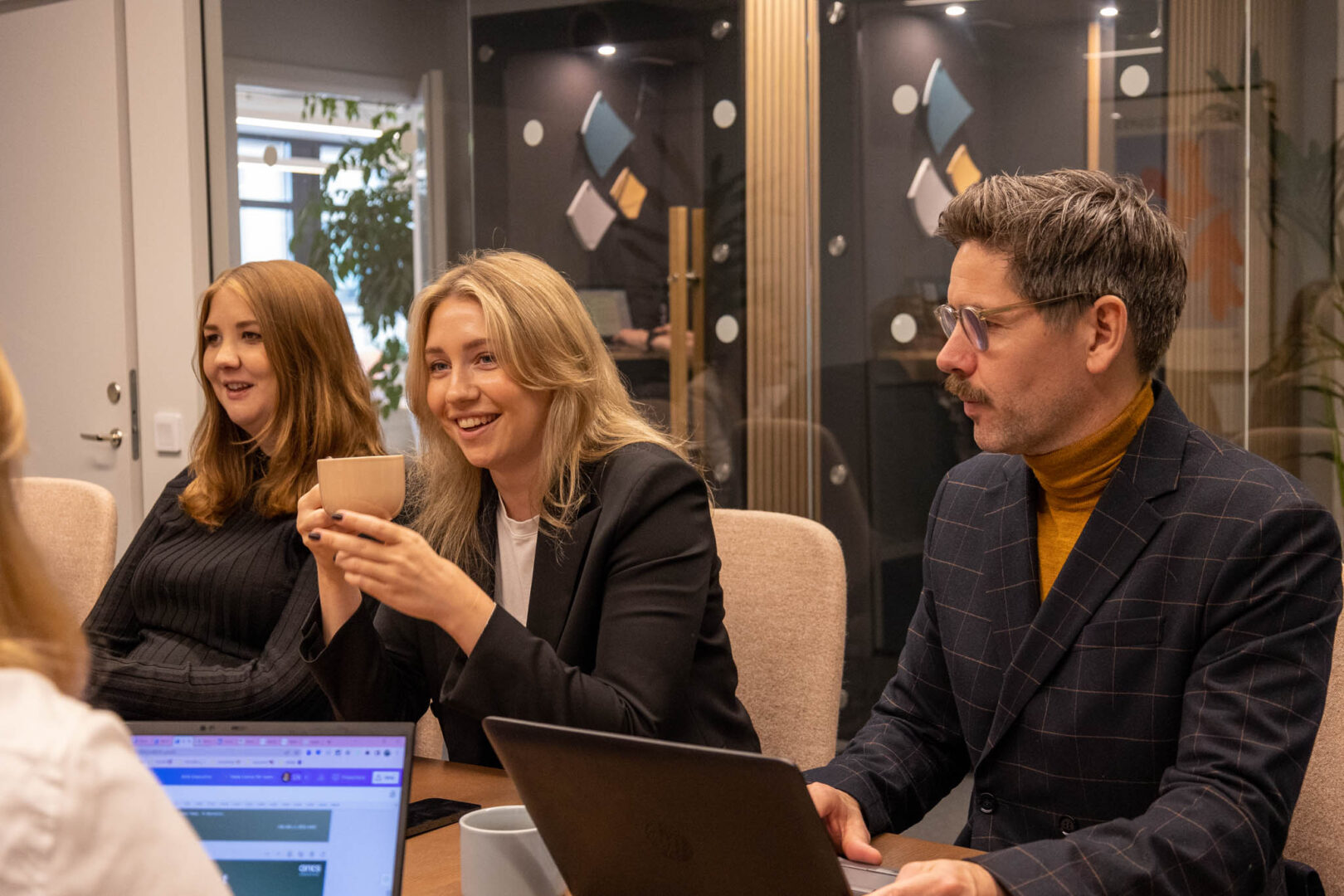 Ett team av chefer, inkl. en Chief Growth Officer, CPO och Tech HR-chef, har en fika och diskuterar strategi och tillväxtmöjligheter för att driva innovation och framgång i deras techföretag, medan de njuter av ett informellt samtal i ett inglasat mötesrum.