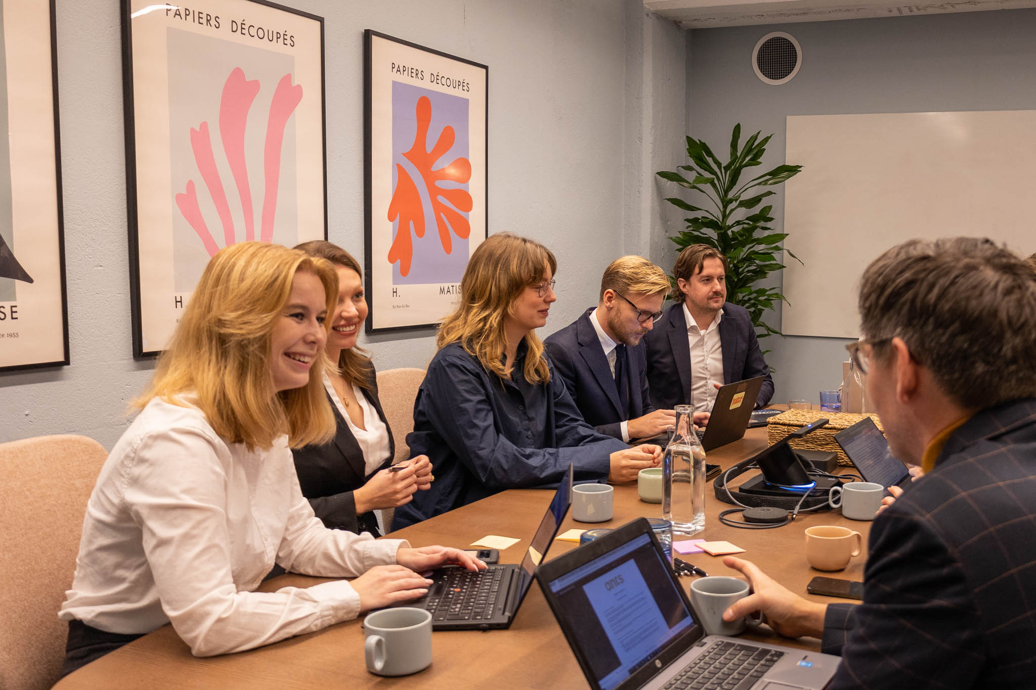 Chefer inom offentlig sektor sitter runt ett bord i ett mindre kontorsrum med abstrakta tavlor bakom sig och pratar om transformation och digitalisering.