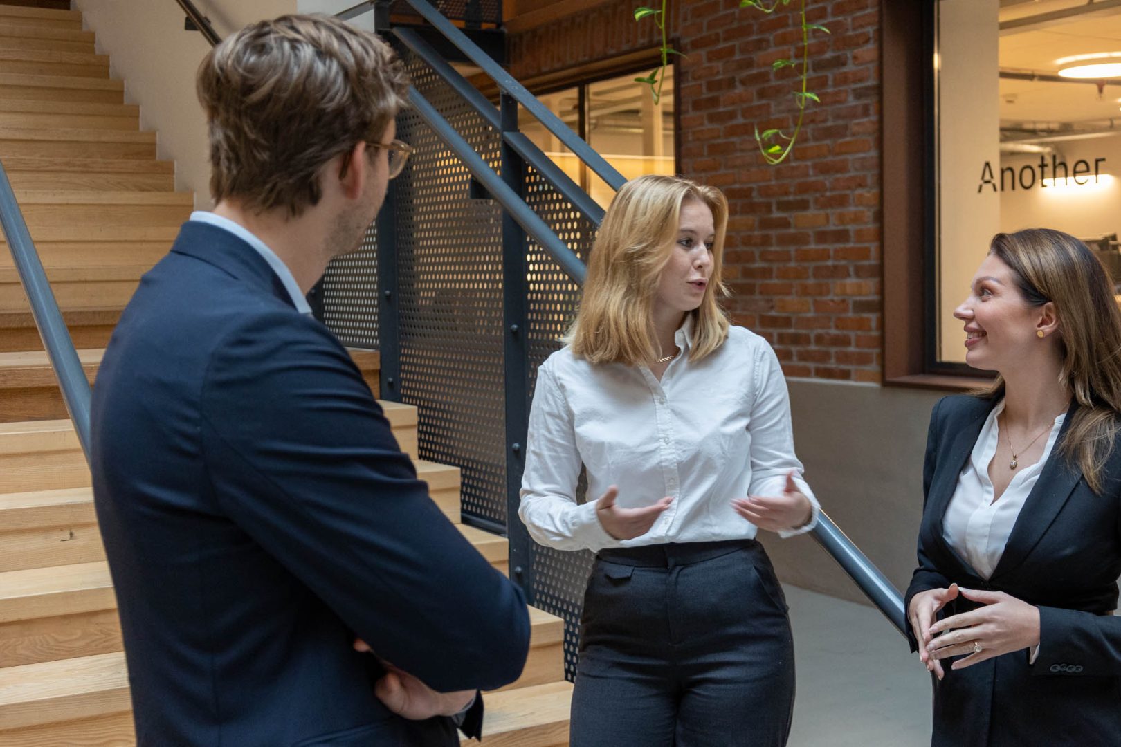 En Chief Technology Officer (CTO), Chief Digital Officer (CDO) och Chief Marketing Officer (CMO) står vid en trappa i trä och diskuterar samarbetet mellan IT och marknadsföring för att driva digital transformation och effektivisering inom tillverknings- och processindustrin.
