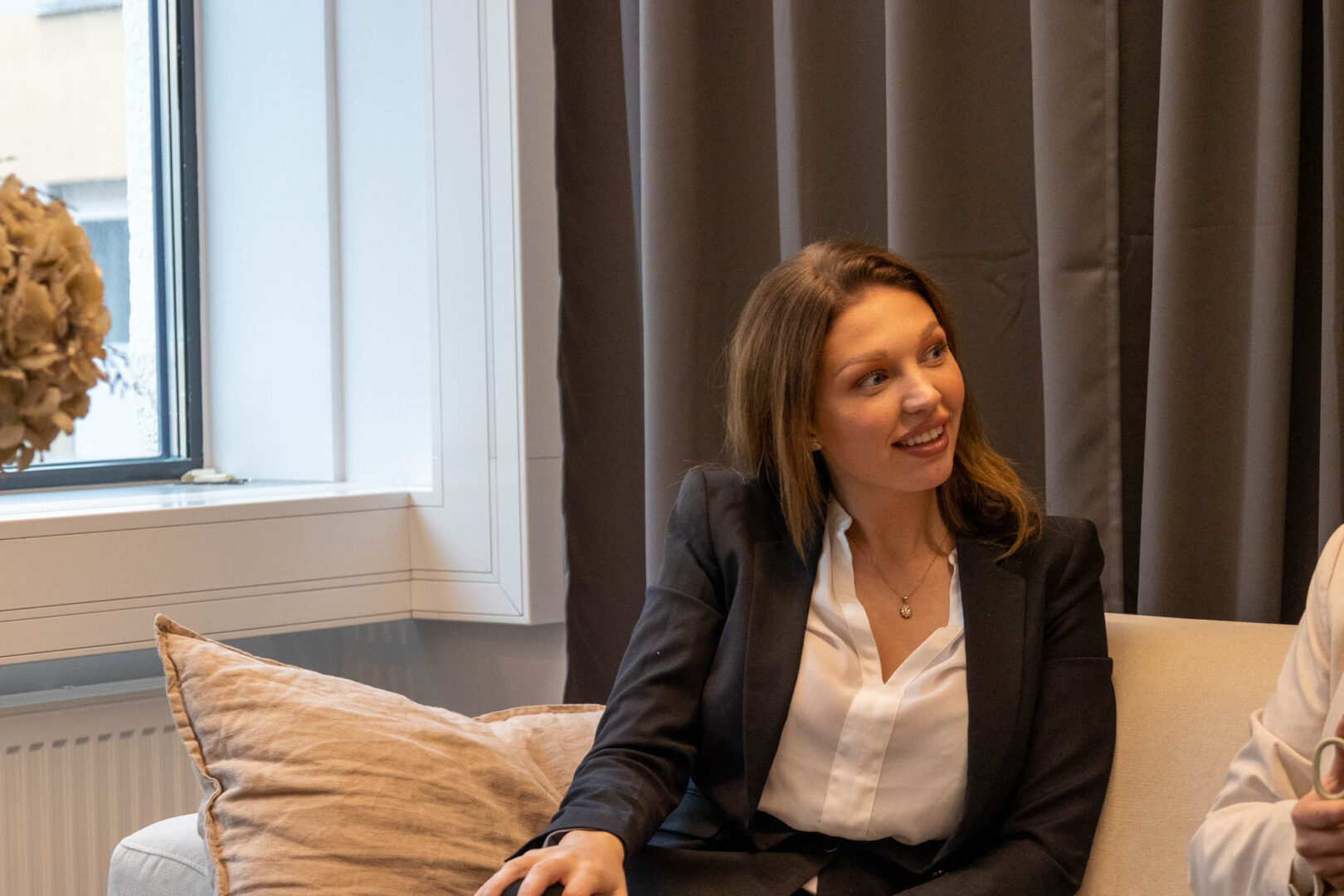 En kvinnlig kategorichef inom detaljhandeln sitter i en beige soffa och ler när hennes kollega pratar om produktstrategier och online merchandising.
