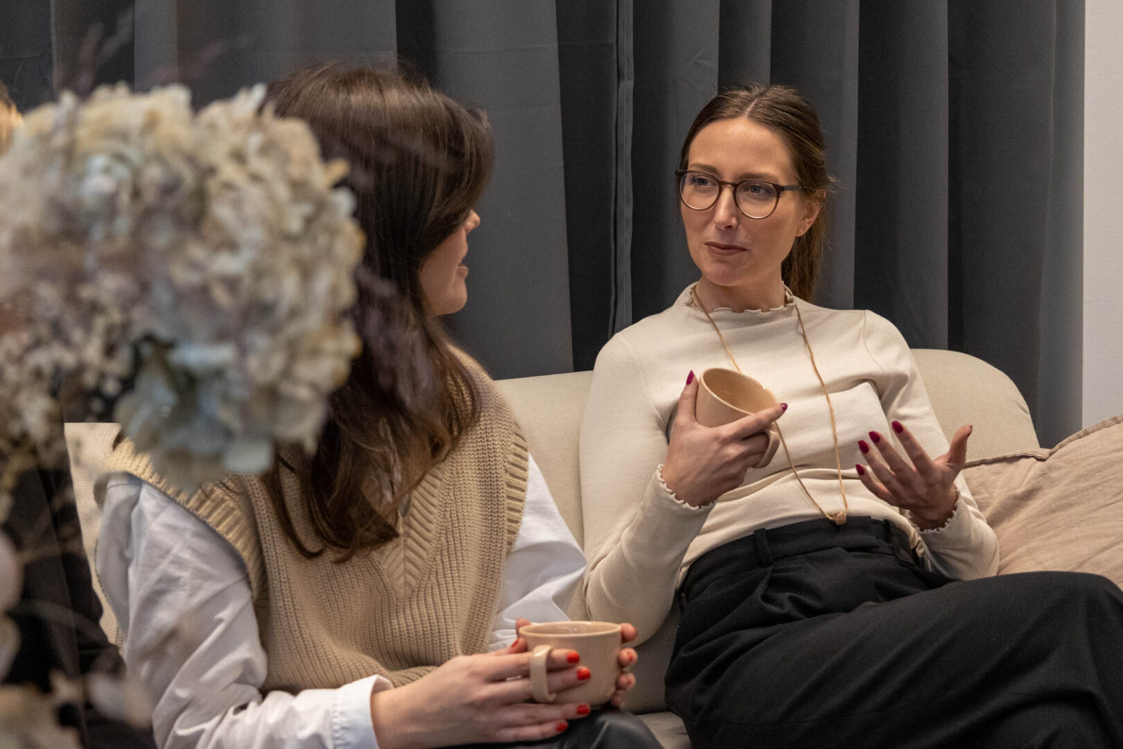 En Chief Financial Officer (CFO) och en Head of Strategy på ett PE-investerat bolag sitter avslappnat i en beige soffa med varsin kopp kaffe och diskuterar affärsstrategier för att optimera affärsprocesser under transformation.