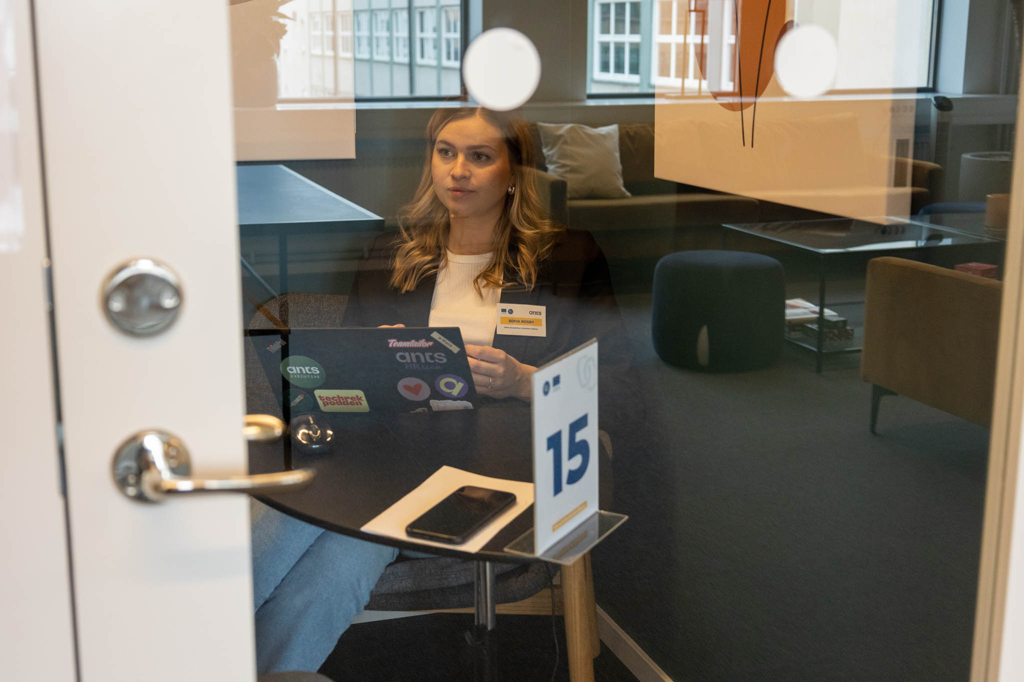 En kommunikatör sitter i ett tyst inglasat rum ensam vid ett svart bord med sin laptop ovanpå och förbereder kampanjer för en ny produkt som ska lanseras på marknaden för att stärka företags cybersäkerhet.